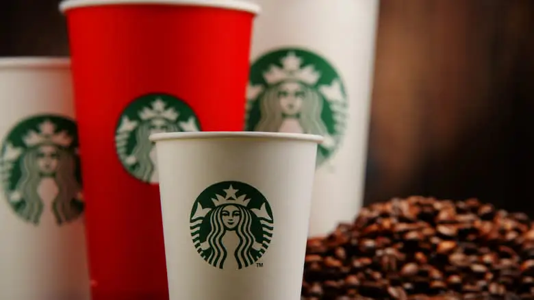 Different sized Starbucks cups next to a pile of coffee beans