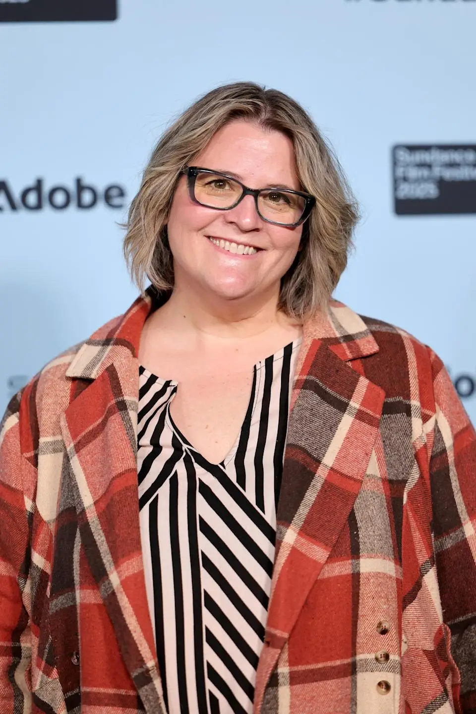 Person smiling in a checkered coat and striped shirt at a film festival event