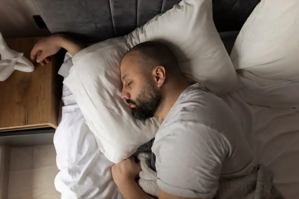 coffee, sleep and brain health: man sleeping in bed with arm under the pillow