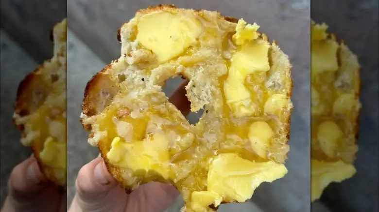 Hand holding a bagel half covered in butter and honey