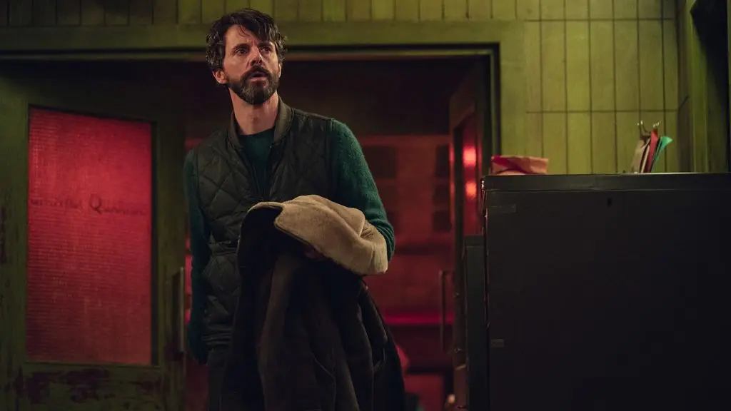 man with beard holding coat in dimly-lit room 