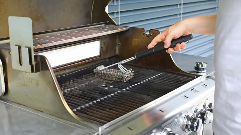 Person using a wire brush to clean grill grates