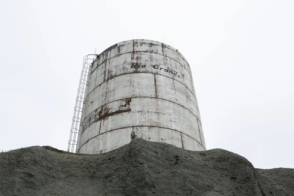 A large, corrugated metal water tank that reads "RIO GRANDE" sits atop a shale hill in Rangely, Colorado.