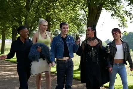 A group of white and black friends walk through a park as if about to go out for the night, with some drinking cans of alcoholic drinks