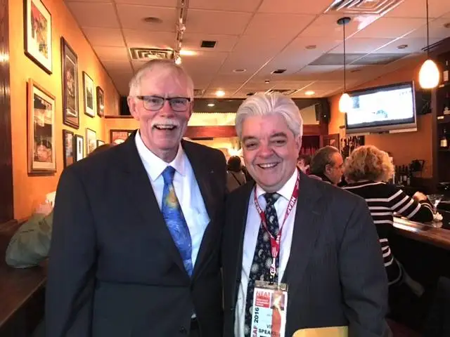 two men in suits smile for a photo in a cafe