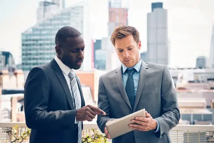 Two people in business attire stand outside and look at a report.