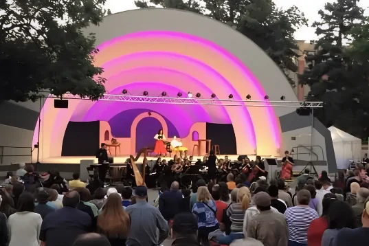 A large crowd sits outside the Boulder Bandshell watching an Opera performance.
