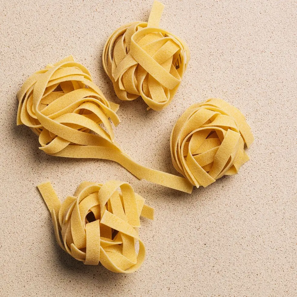 raw uncooked fettuccine pasta nests on beige background