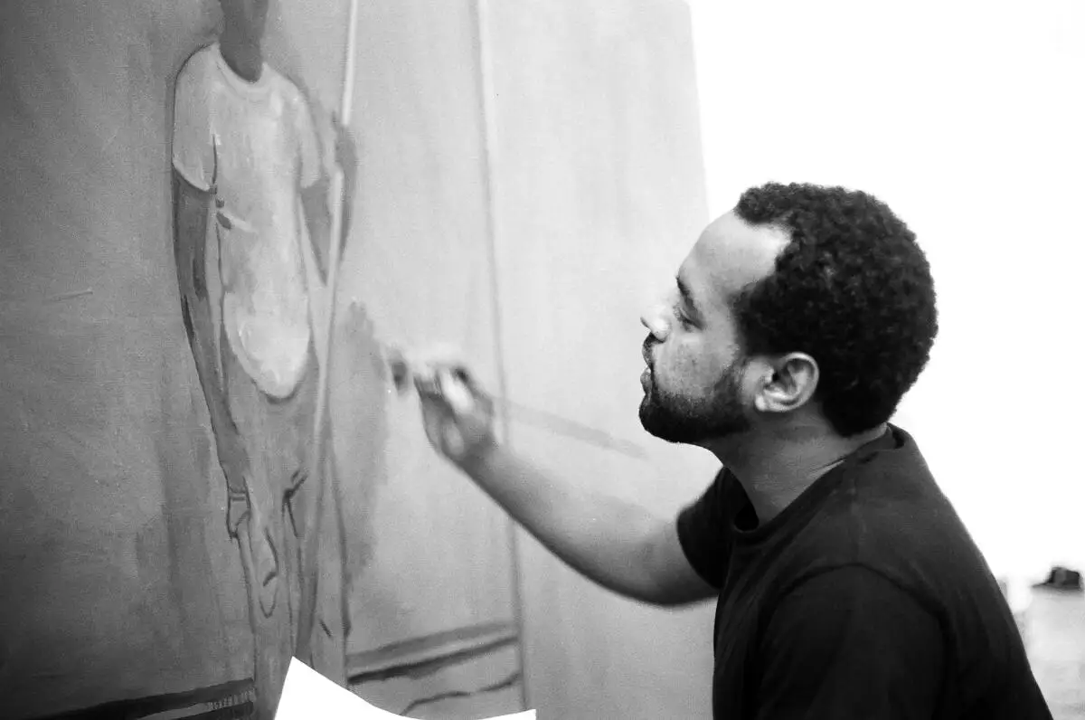 A beareded young Black man paints a figure on a canvas.