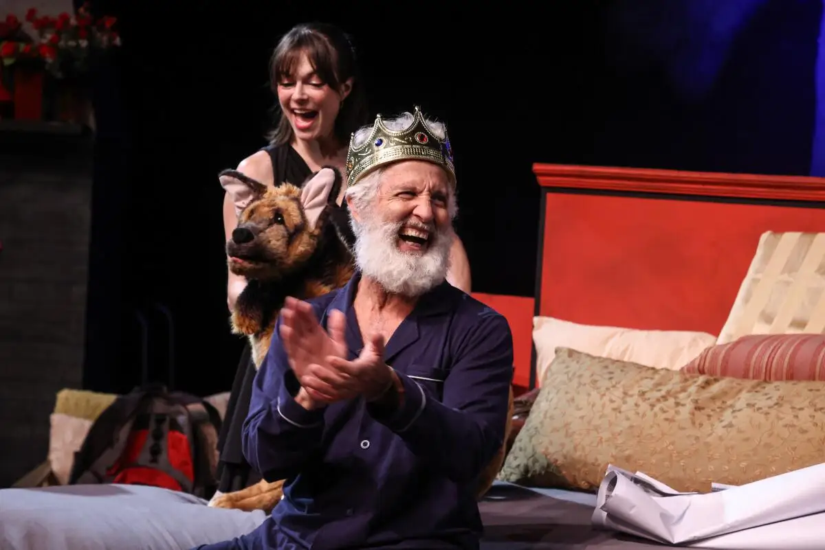 A man wearing a crown claps and laughs.