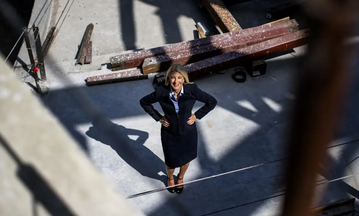 A woman with her hands on her hips stands in a construction site looking up. 