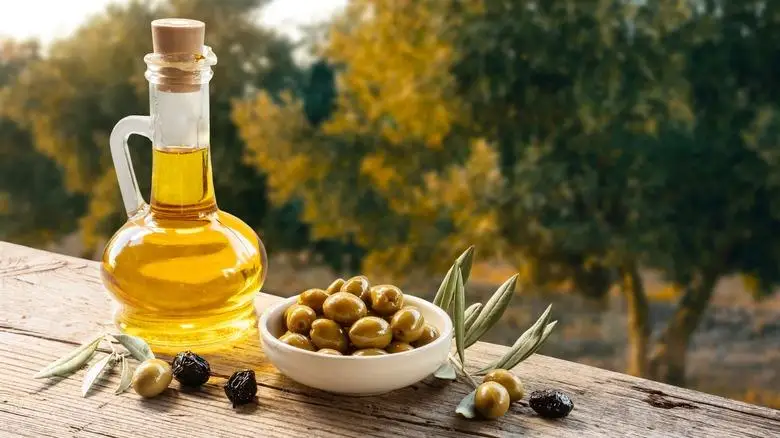 Bottle of olive oil, olive leaves, and olives on wooden outdoor table