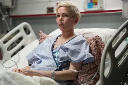 A white female patient with cropped blonde hair is in a hospital bed and connected to a respirator by tubes