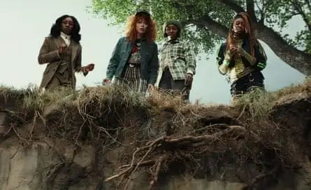 Three black women and one white woman look over a grassy bank with a tree behind them
