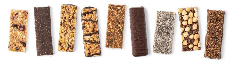 Nine different unwrapped granola bars, some of which have chocolate coating or drizzle.