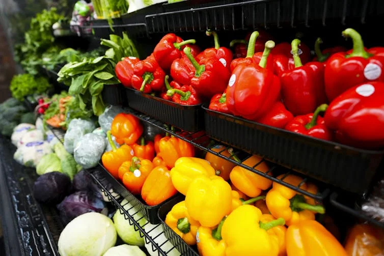 The produce aisle at a supermarket, showing fresh bell peppers and lettuce.