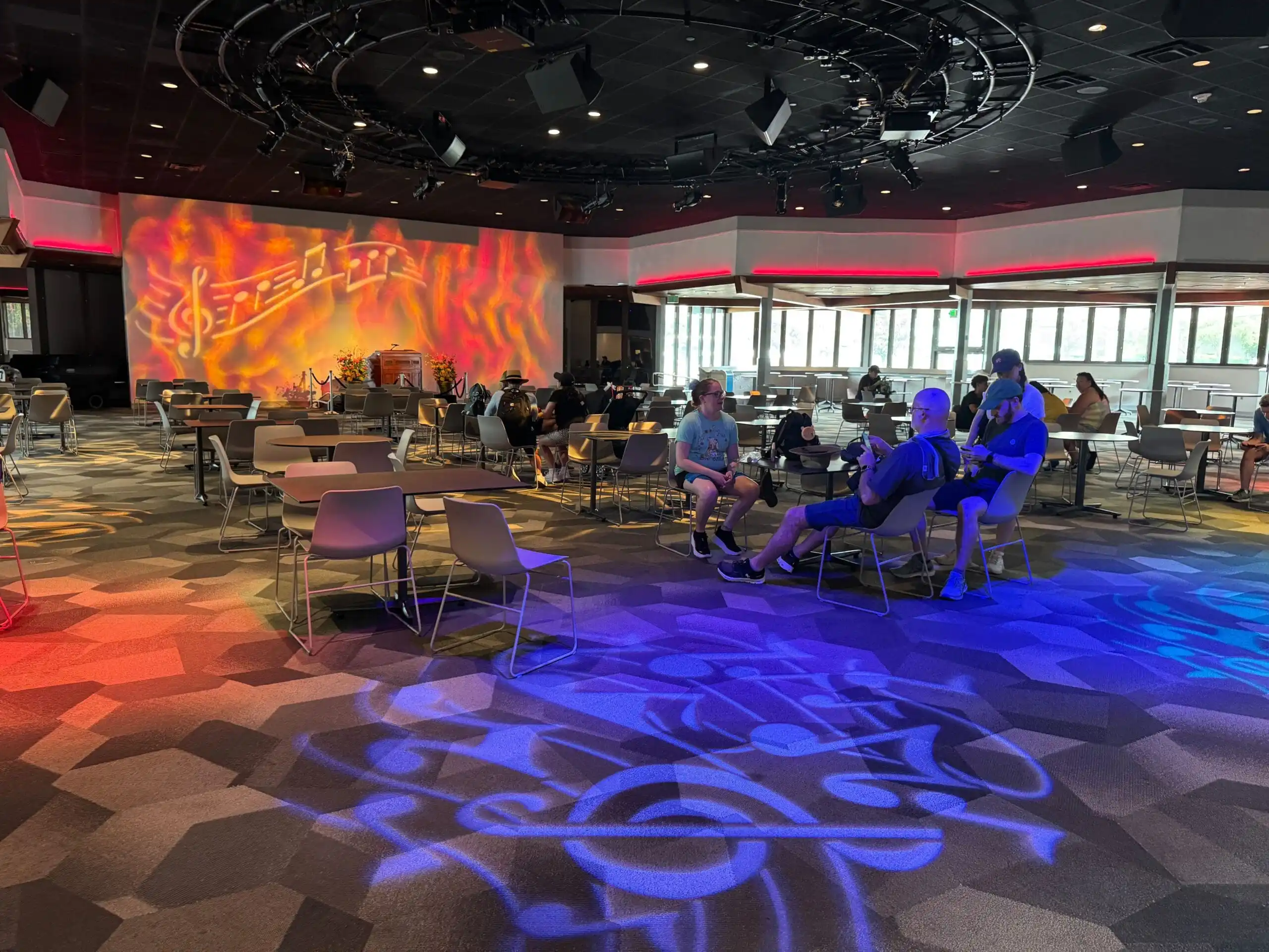 A modern lounge at EPCOT with colorful musical note lights; guests enjoy chatting and new entertainment.