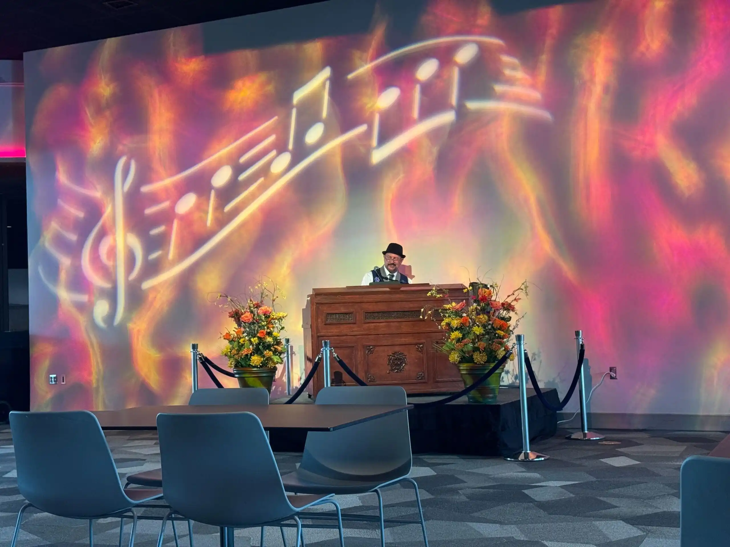 An EPCOT performer in a hat plays an organ onstage as colorful musical notes dance across the wall behind him.