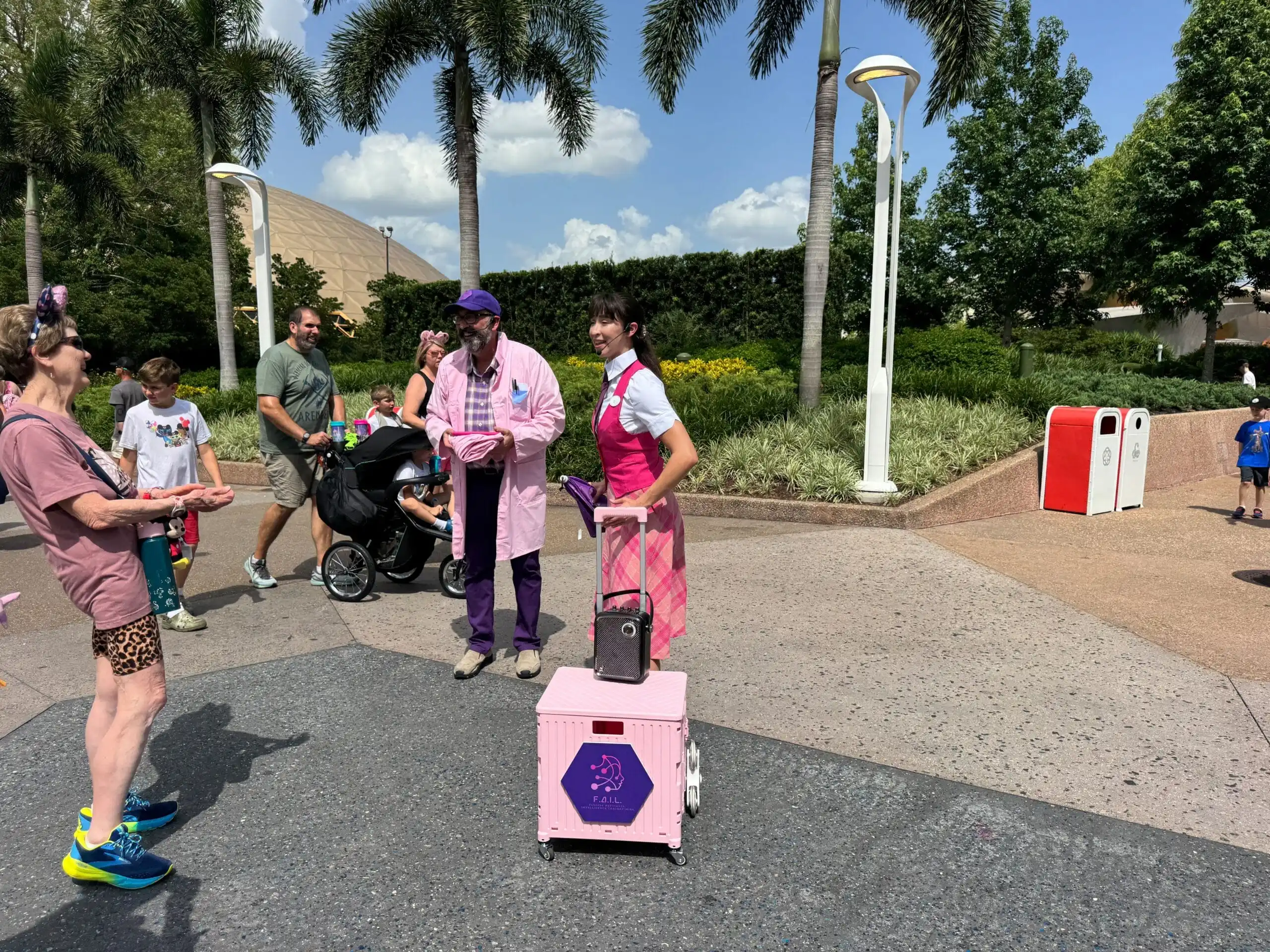 Two people in pink uniforms stand by a pink cart at EPCOT, handing out treats to passersby in a park.