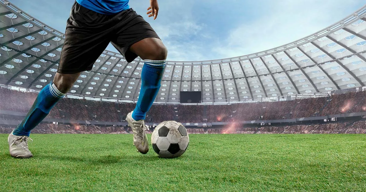 Fotomontagem que mostra um jogador de futebol, do qual só se veem as pernas e a bola, num estádio de futebol.