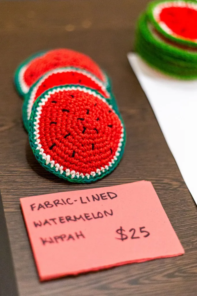 a close up of a wooden table where kippahs are for sale. They are knit to look like round slices of watermelon.