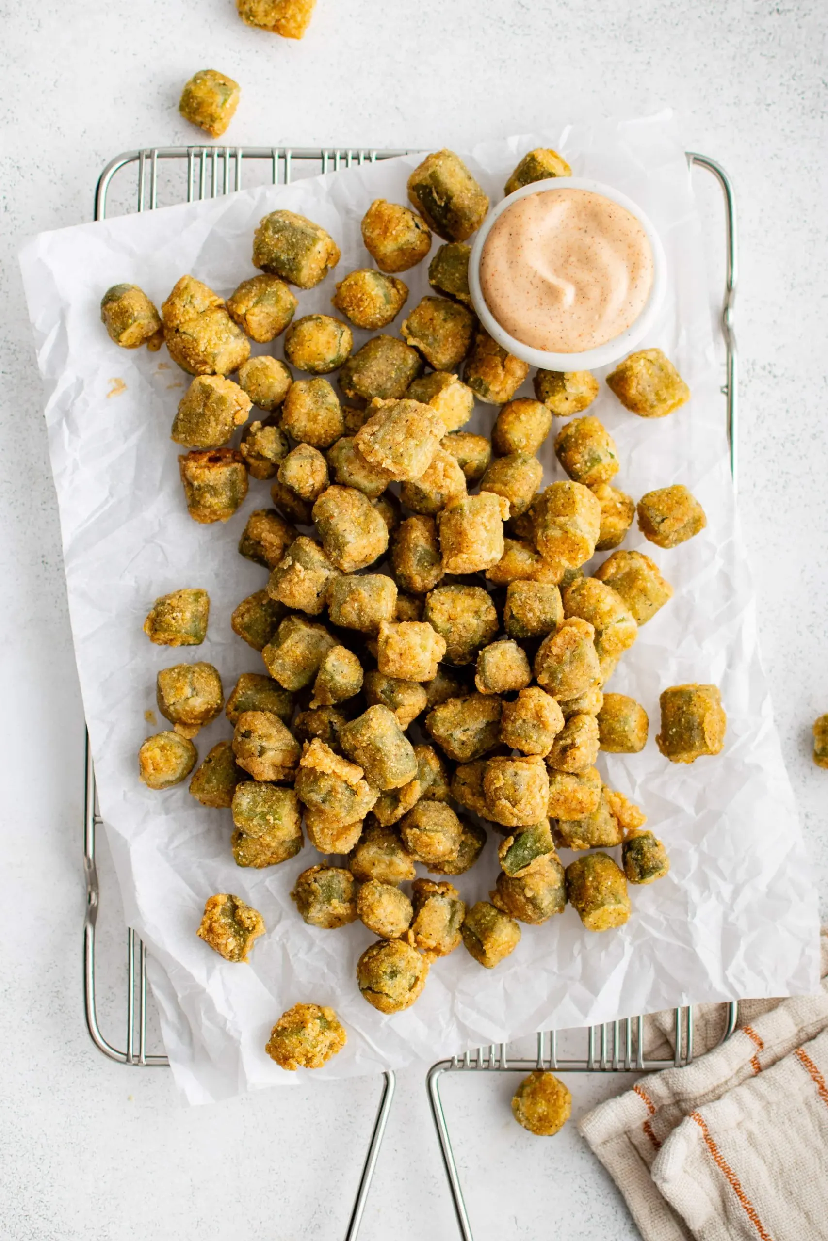 Perfectly golden and crispy deep-fried okra on a large piece of parchment paper set over a wire rack and served with a creamy mayo sauce for dipping.