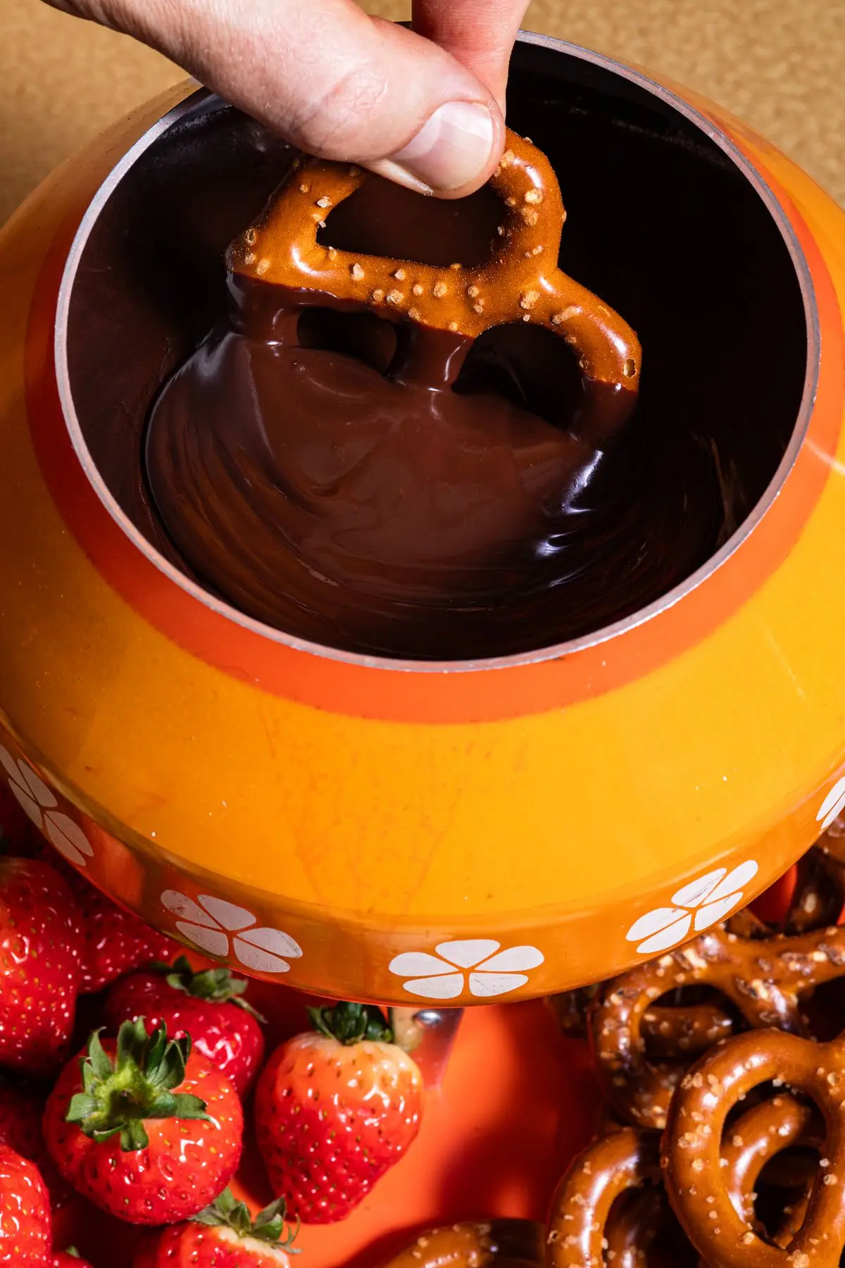 Hand holding pretzel dips it into a pot of chocolate fondue.