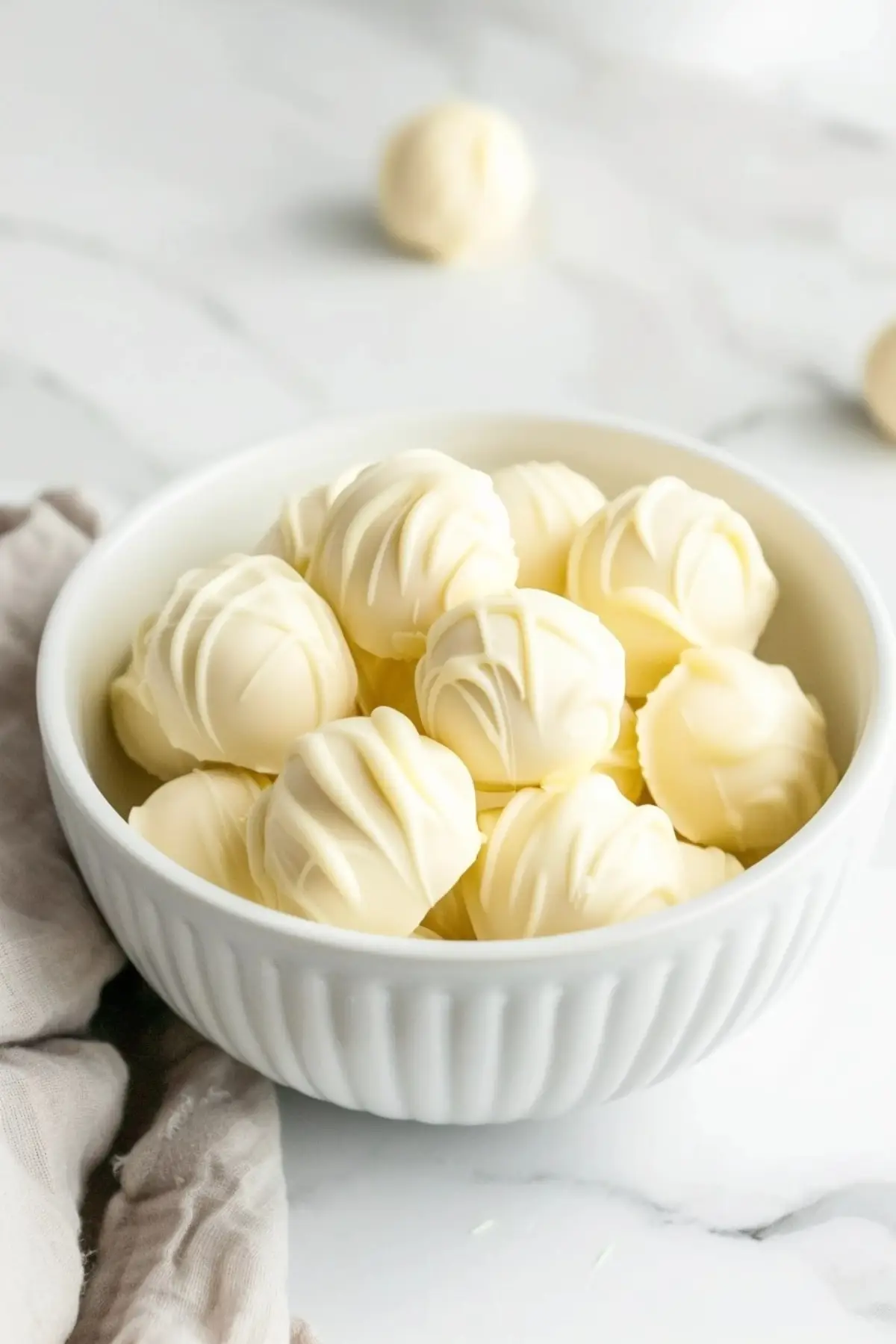 Chocolate truffles coated in white chocolate served on a bowl on top of a white marble table.