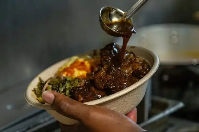 Chef and owner Boris Seymore plates a soul bowl containing collard greens with smoked turkey, Mac & Cheese, and 'Auntie Loretta's Oxtails' during the opening of his new restaurant, Georgia Mae's, in West Palm Beach, Fla., on October 4, 2023.