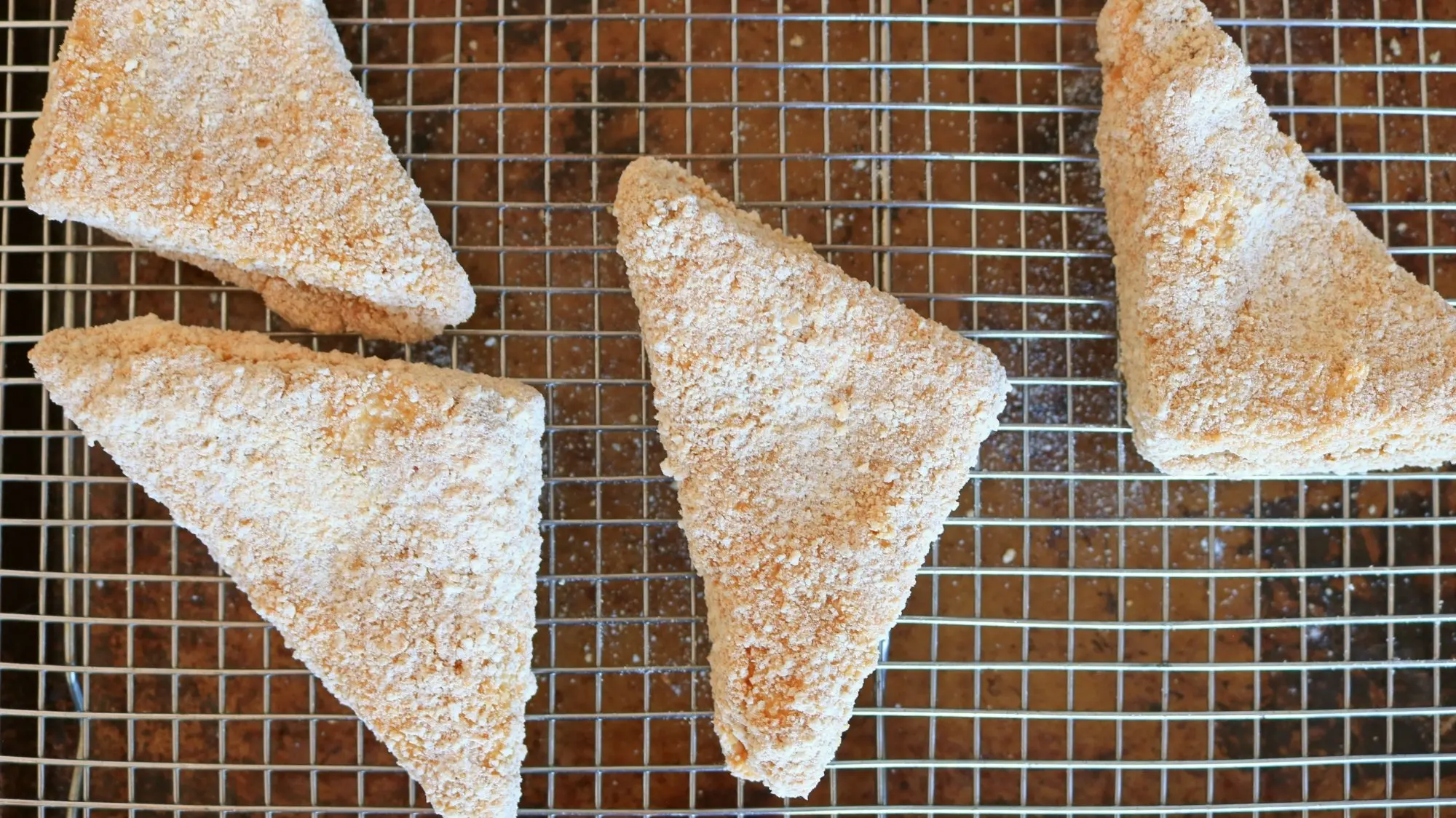 Triangles of breaded sandwiches on a wire rack.