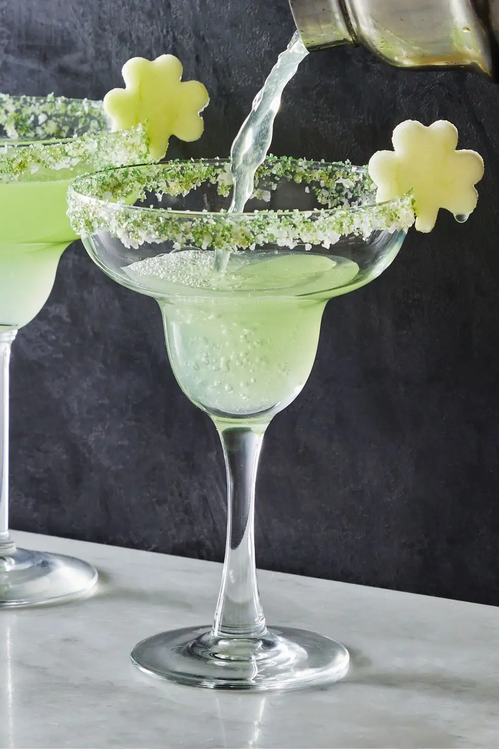 light green shamrockarita cocktail in a sugar rimmed glass with an apple slice shaped like a shamrock as garnish