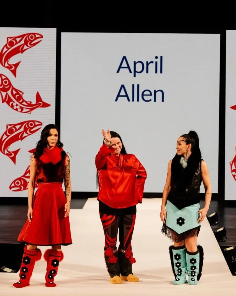 Three women standing on a stage, two in bright red and the other in light green.