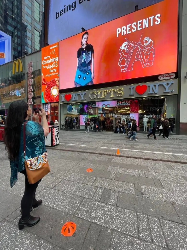A woman takes a photo of a billboard in New York, depicting an Inuit model wearing a fashionable dress.