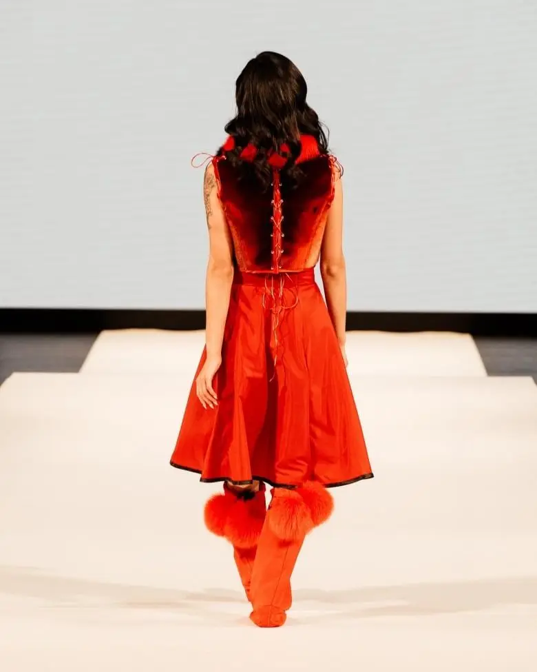 Woman in red dress and fur, from the back, walking on a stage.