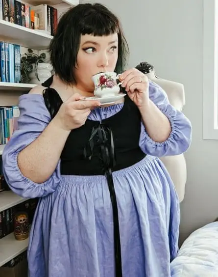 Amy Ludvik in a purple dress drinking a cup of tea