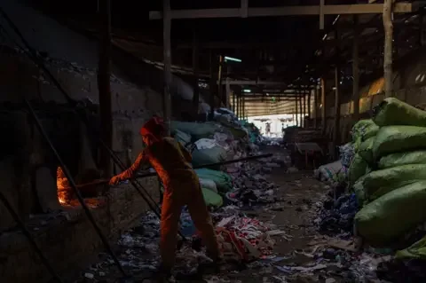 Thomas Cristofoletti/ BBC A woman feed the fire in the kiln