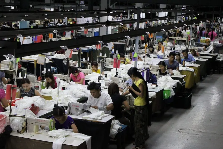 Workers sit at tables sewing clothes.