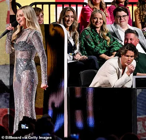 The audience jumped to their feet to cheer on the songstress, including Chase who could be seen holding a bright smile on his face while supporting his girlfriend as she took on hosting duties