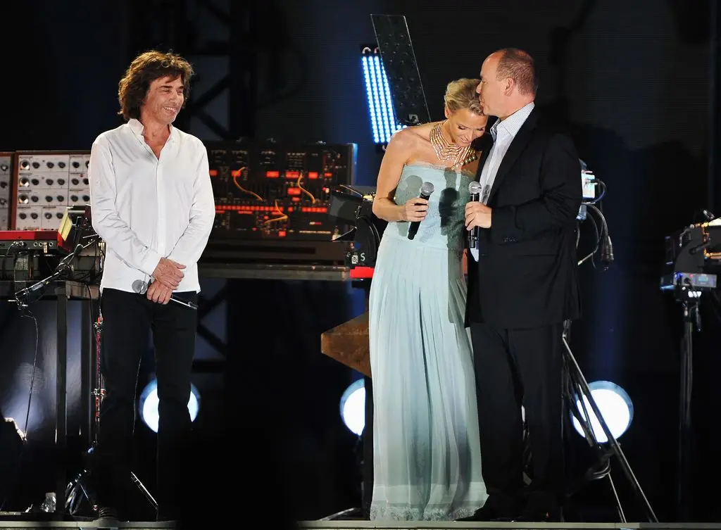 Princess Charlene of Monaco in a blue outfit leaning into Prince Albert II of Monaco appear onstage during the Jean Michel Jarre wedding concert