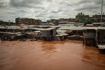 Tin shacks half-submerged by brown flood water