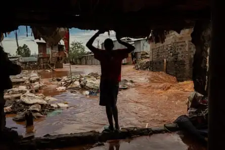 The silhouette of a man standing in a big hole where there was a wall, looking at flood water sweeping by outside