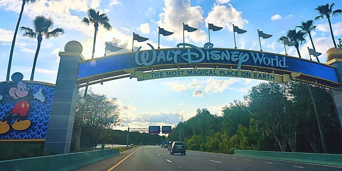 A large, colorful archway sign welcomes visitors to Walt Disney World, featuring its iconic slogan 