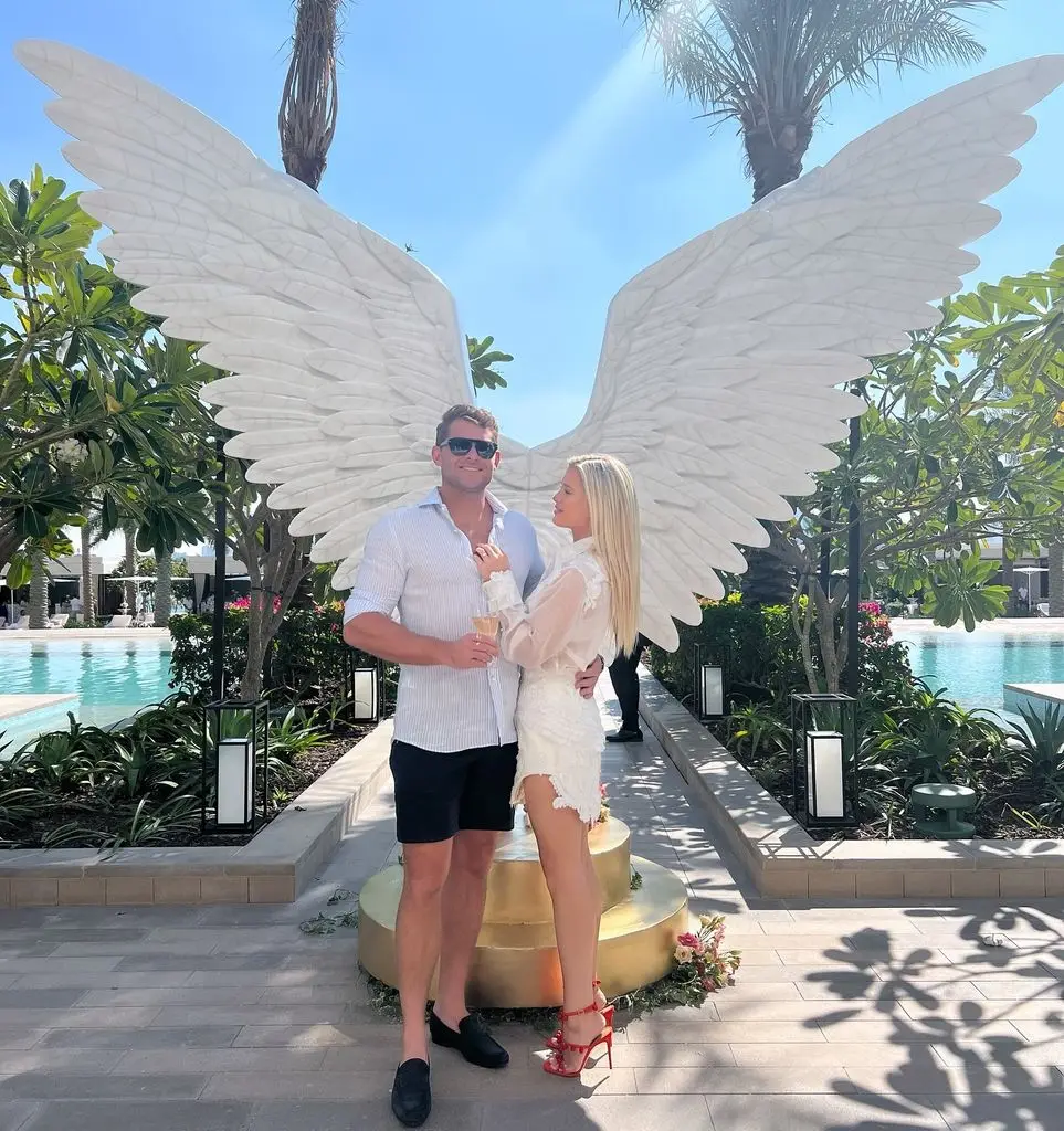 Amelia Spencer and Greg Mallett in front of angel wings by pool