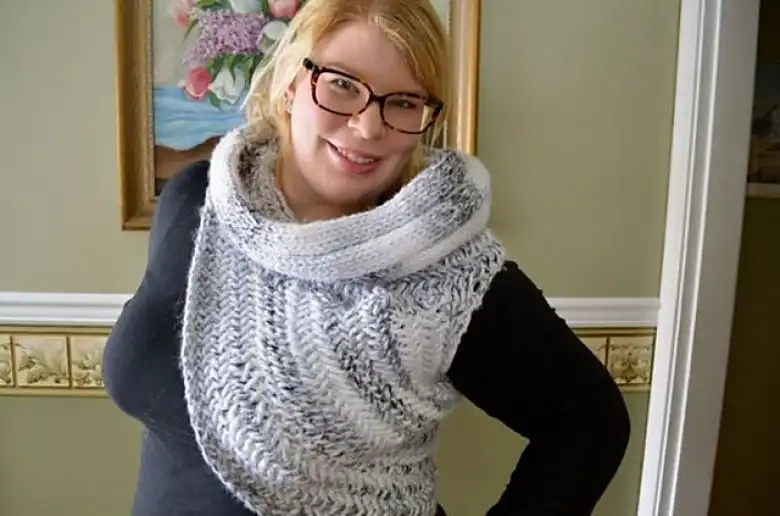 A smiling woman poses while wearing a white and grey knitted vest with one shoulder.