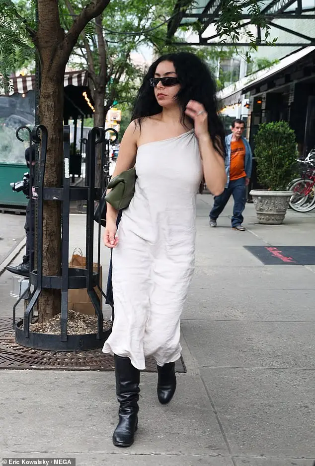 Charli XCX cut a stylish display in a one shoulder white dress and black boots as as she left her hotel in New York on Tuesday afternoon