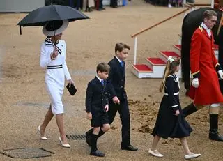 Catherine, Princess of Wales, shelters from the rain with an umbrella as she walks with her children Britain's Prince George of Wales (C), Britain's Princess Charlotte of Wales (R) and Britain's Prince Louis of Wales back to the Glass State Coach at Horse Guards Parade during the King's Birthday Parade 