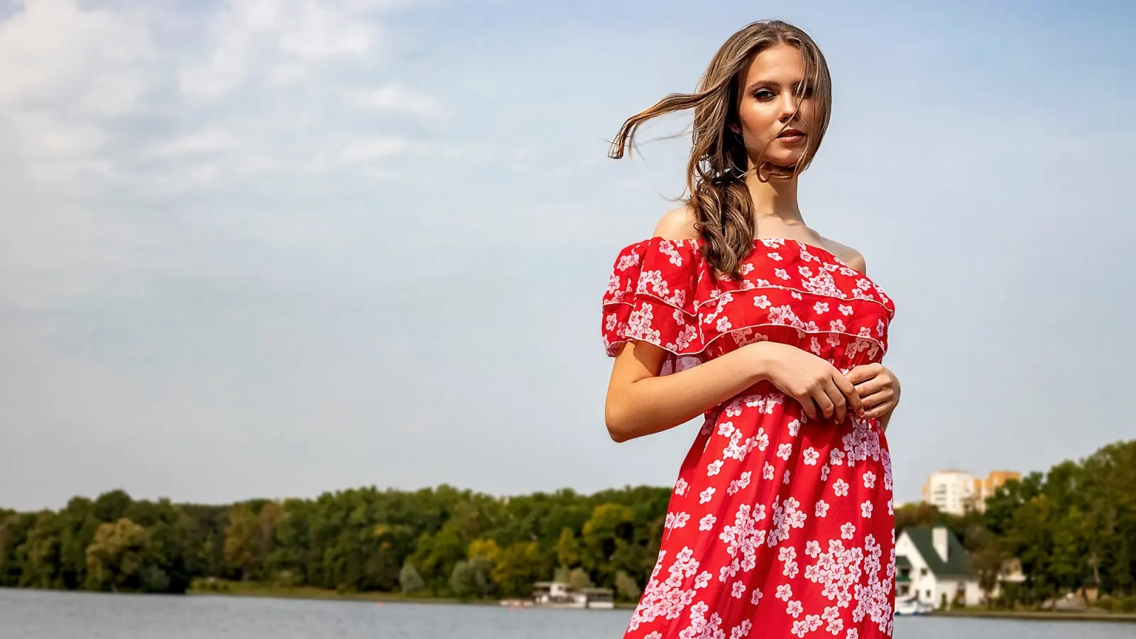 Portrait of a beautiful young brown-haired girl with long hair in a red dress on a lake background. Belarus