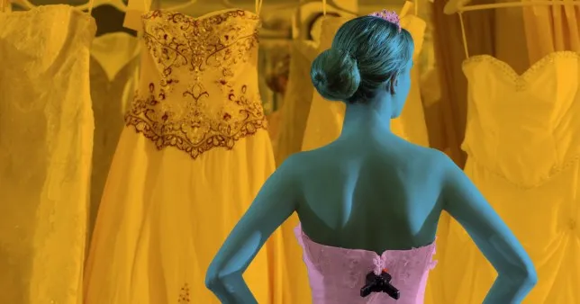 A woman standing wearing a wedding dress, looking at all other dresses in front of her