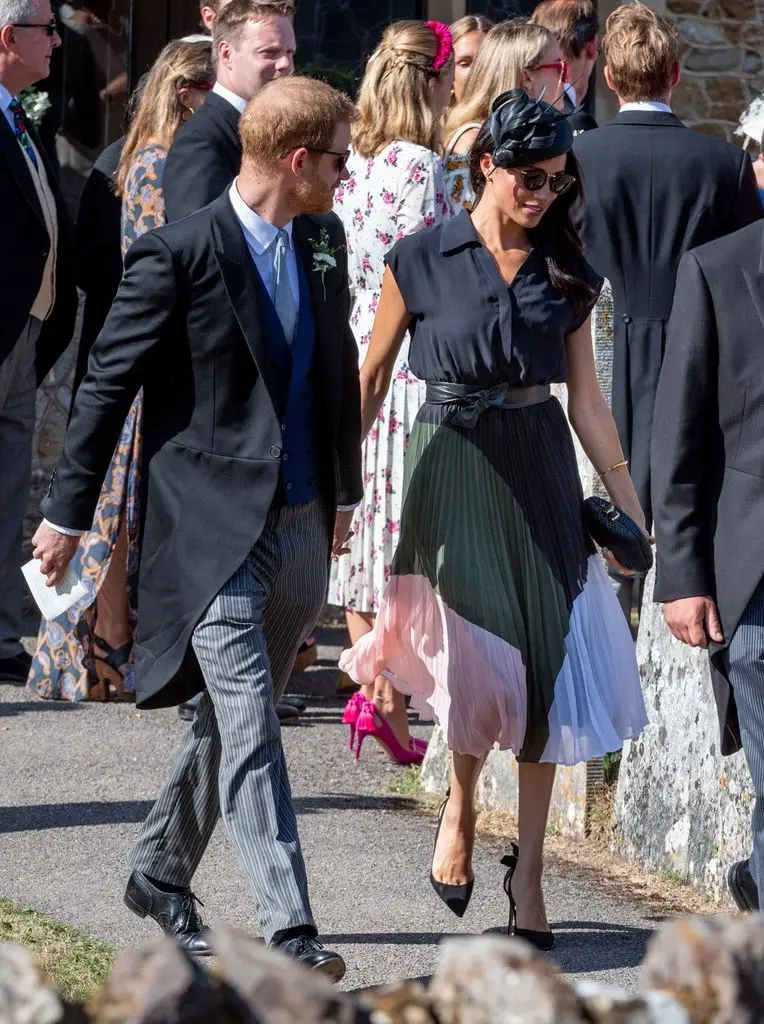 Meghan Markle in a pleated dress holding hands with Prince Harry