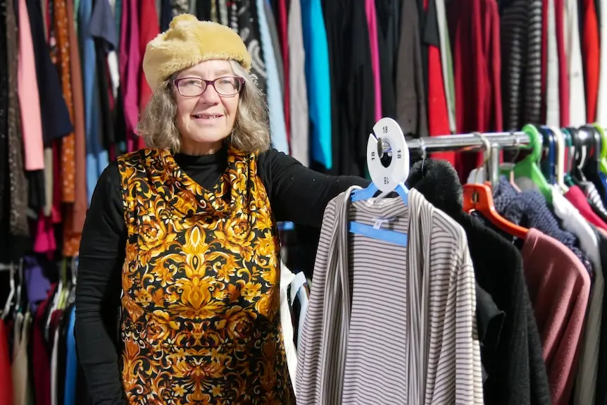 A woman standing next to a clothing rack at an op shop.